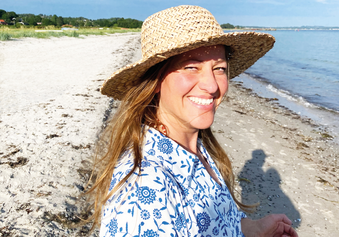 Smilende kvinde med stråhat på stranden